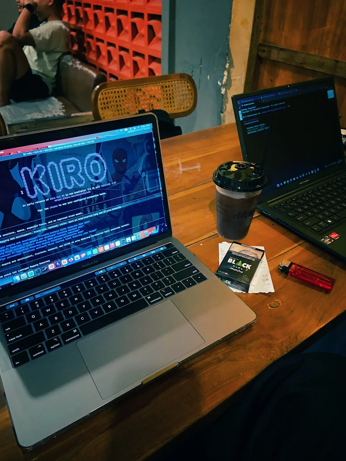 Two laptops on a café table, one of them running Kiro CLI